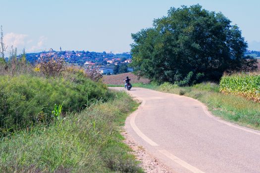 Solitary biker riding over empty road between the hills