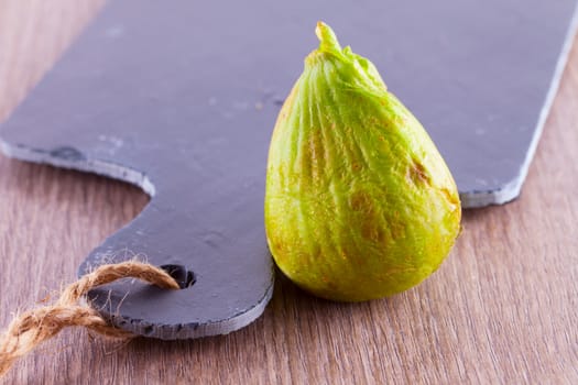 Green fig standing near a black chopping board
