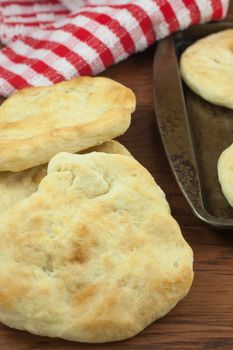 Homemade pita bread sitting on a wooden table with a red cloth in the background.