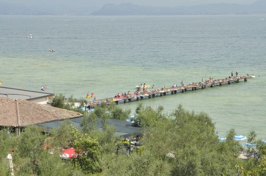 People sunbathing on wooden pier  in Sirmione, located in the lake Garda, Italy