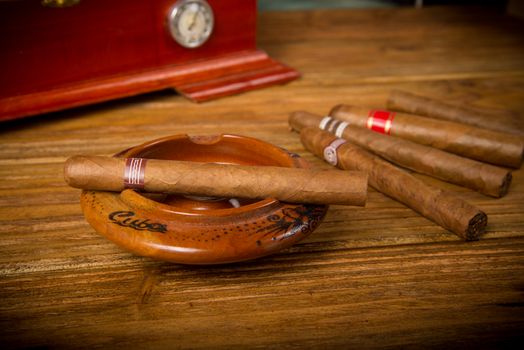 Cuban cigars and humidor with ashtray on rustic wooden table