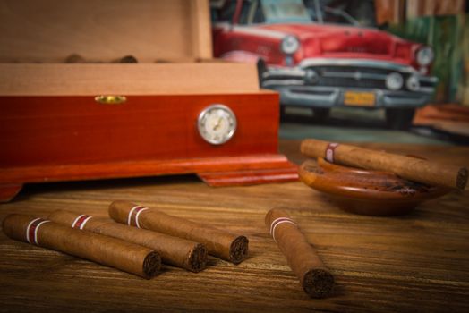 Cuban cigars and humidor with ashtray on rustic wooden table with Cuban painting of american old car in background
