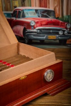Cuban cigars and humidor on rustic wooden table with Cuban painting of american old car in background