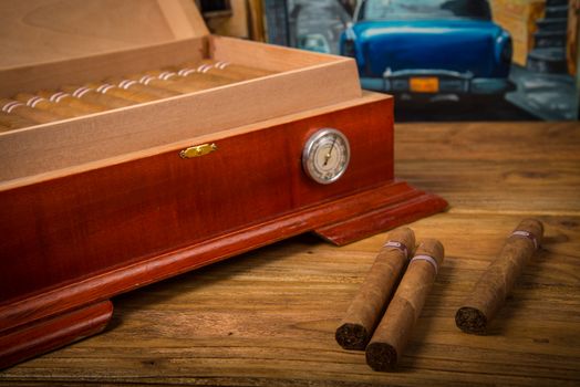 Cuban cigars and humidor on rustic wooden table with Cuban painting of american old car in background