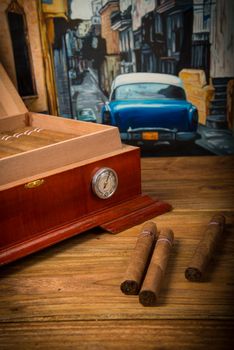 Cuban cigars and humidor on rustic wooden table with Cuban painting of american old car in background