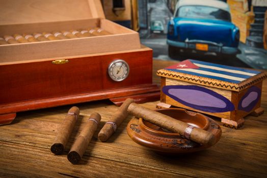 Cuban cigars and humidor with ashtray on rustic wooden table with Cuban painting of american old car in background