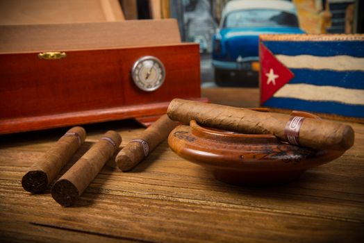 Cuban cigars and humidor with ashtray on rustic wooden table with Cuban painting of american old car in background