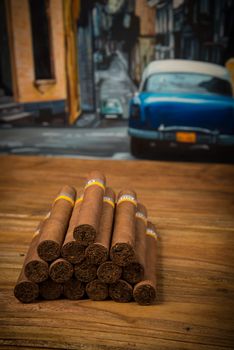 Cuban cigars  on rustic wooden table with Cuban painting of american old car in background