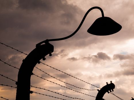 Lamp silhouette in concentration camp. It is part of barwire fence.