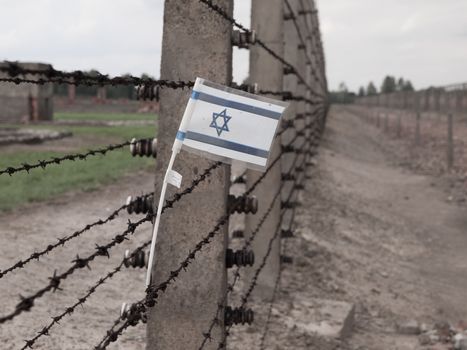 Small flag of Israel hanging on the barbwire in concentration camp