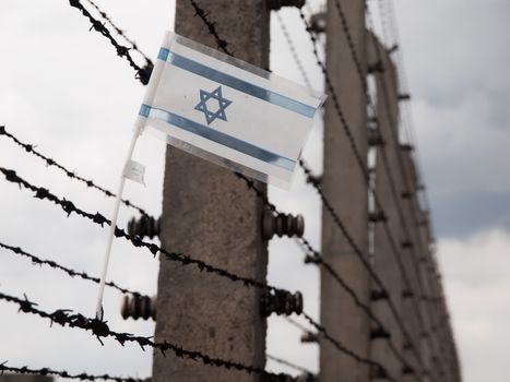 Small flag of Israel hanging on the barbwire in concentration camp