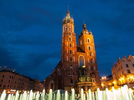 St. Mary's Church with two different towers by night (Krakow, Poland). Viewed from fountain.