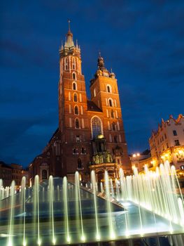 St. Mary's Church with two different towers by night (Krakow, Poland). Viewed from fountain.