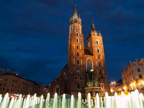 St. Mary's Church with two different towers by night (Krakow, Poland). Viewed from fountain.