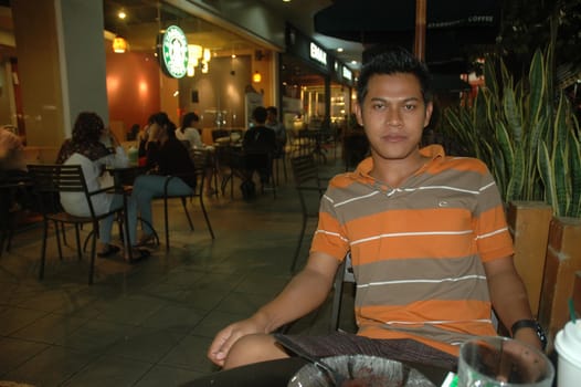 Bandung, Indonesia - July 2, 2011: Young man sit down on chair beside starbuck cafe.