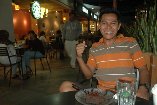 Bandung, Indonesia - July 2, 2011: Young man sit down on chair beside starbuck cafe.