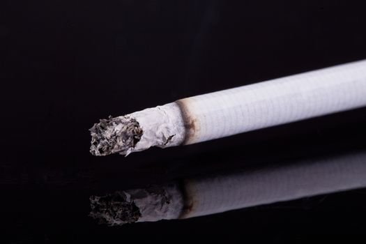 single burning cigarette with ash isolated on black background