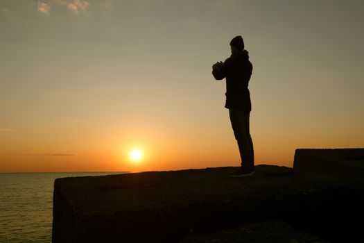A man taking a photo of the sunset with his phone