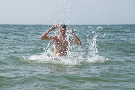 A teen boy splashing water at the beach