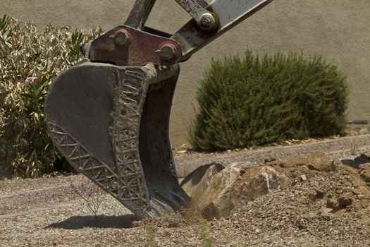 Buiding and construction machinery, a big digging bucket with steel fork, rips up rocks to begin building a new pool or patio