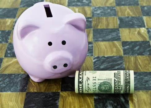 Pink savings bank with rolled American dollar placed on game board reflects feminine financial decisions and actions; 