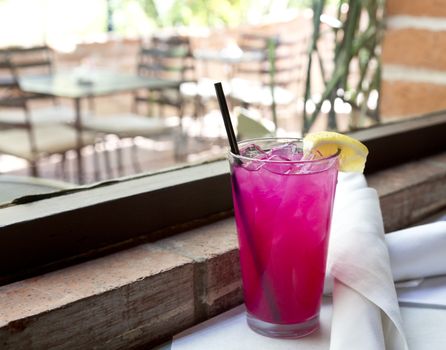 Pink lemonade with ice, lemon wedge, and black straw in tall glass by patio window with rustic,  brick sill. Location is America's Southwest, Tucson, Arizona.