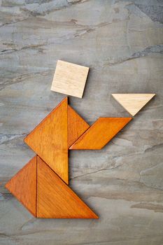 abstract picture of a figure offering a cup of tea or soup built  from seven tangram wooden pieces against slate rock, a traditional Chinese puzzle game, the artwork copyright by the photographer