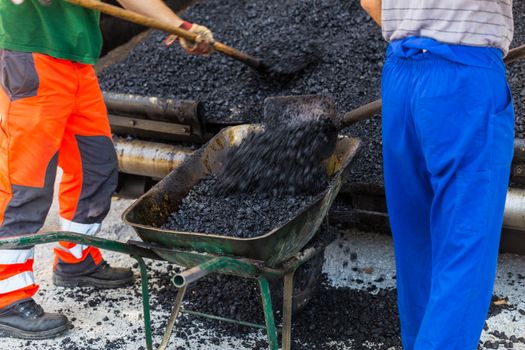 Construction workers during asphalting road works wearing coveralls. Manual labor on construction site.