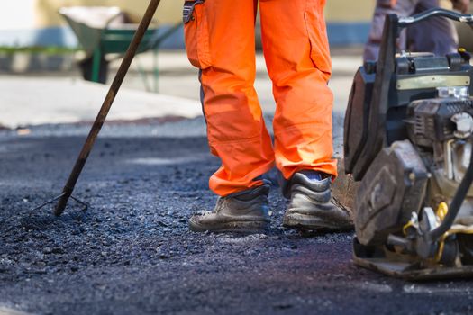 Construction workers during asphalting road works wearing coveralls. Manual labor on construction site.