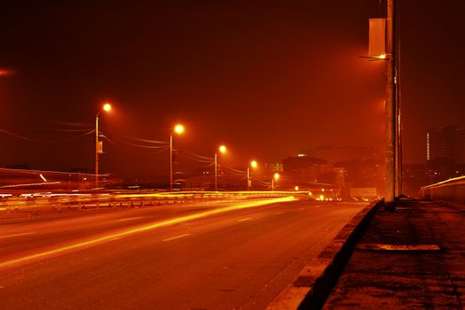 Night view of road in city. Bridge over river, lights on poles