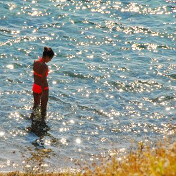 girl in orange swimsuit over sunny shining sea water