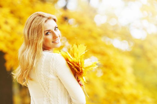 Smiling beautiful young woman with bunch of leaves in autumn park