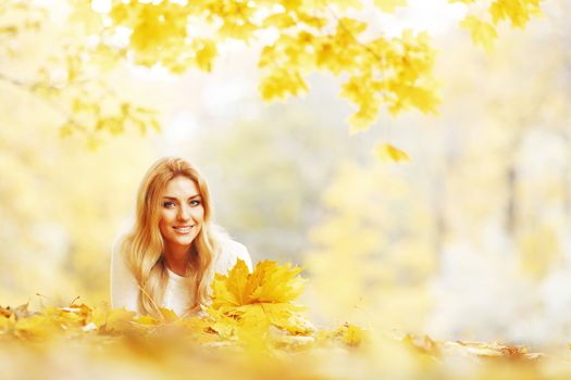 Young woman laying down on the ground covered dry autumnal foliage in beautiful park