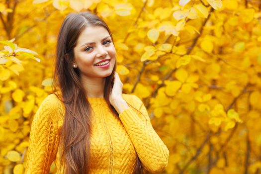 Young smiling brunette posing in autumn park on yellow trees background