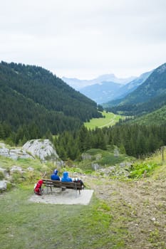 LA BALME, FRANCE - AUGUST 25: Hikers doing the Mont Blanc tour resting on bench in La Balme overlooking La Rollaz. The tour crosses France, Italy and Switzerland. August 25, 2014 in La Balme.