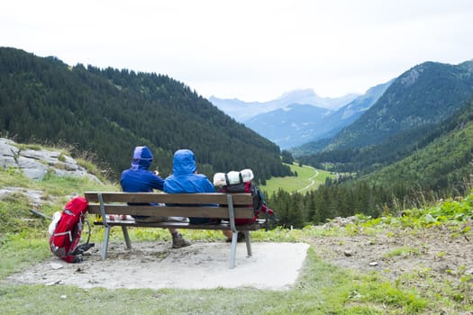LA BALME, FRANCE - AUGUST 25: Hikers doing the Mont Blanc tour resting on bench in La Balme overlooking La Rollaz. The tour crosses France, Italy and Switzerland. August 25, 2014 in La Balme.