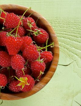 Perfect Ripe Raspberries with Stems in Wooden Bowl on Light Green Wooden background. Top View