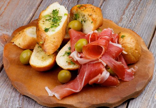 Arrangement of Delicious Tapas with Smoked Jamon, Garlic Bread and Green Olives on Wooden Plate isolated on Rustic Wooden background