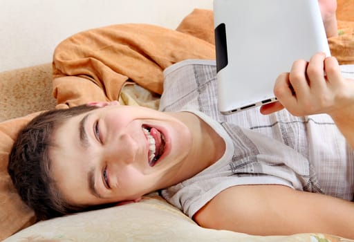 Cheerful Teenager with the Tablet Computer on the Sofa at the Home