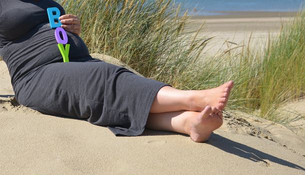 adult pregnant woman holding her hands on her belly on the beach with sand and sea