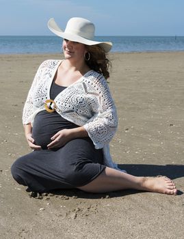 adult happy pregnant woman sitting on the sand beach with sea as background