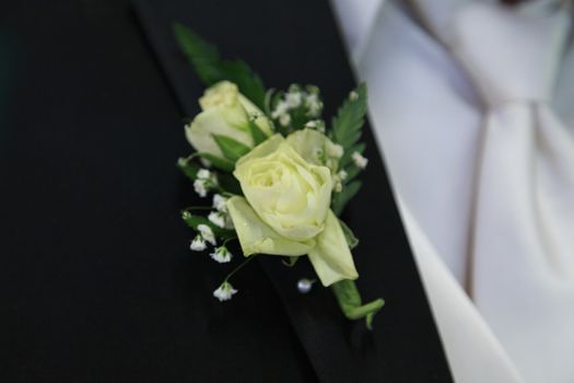 Off white flowers of this grooms boutonniere are pinned to his black lapel. 
