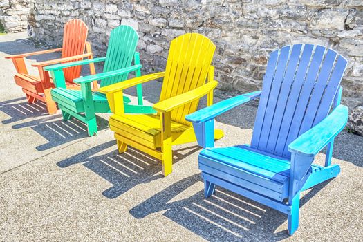 Brightly colored adirondack chairs arranged in a row. Bright sun lights them.