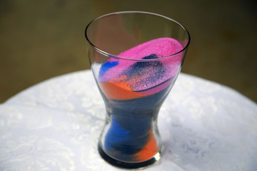 Colorful sand including pink, blue, and orange inside a glass vase. 
