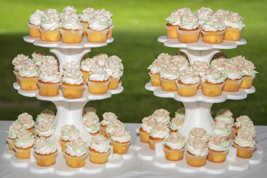 Two towers of beautiful delicious cupcakes sit on top picnic table. 