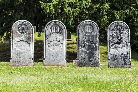 Four weathered and historic headstones in a row. Classic gravestone shape. 