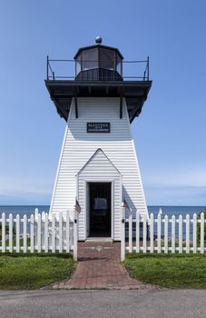 Cute historic and small lighthouse with white picket fence. A brick walk leads to an open door. 