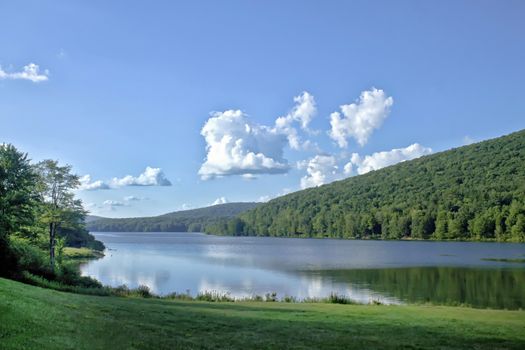 Green mountains surround this placid lake on a blue and clear day in the country. 
