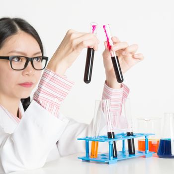 Asian lab worker doing blood test analysis, on plain background.
