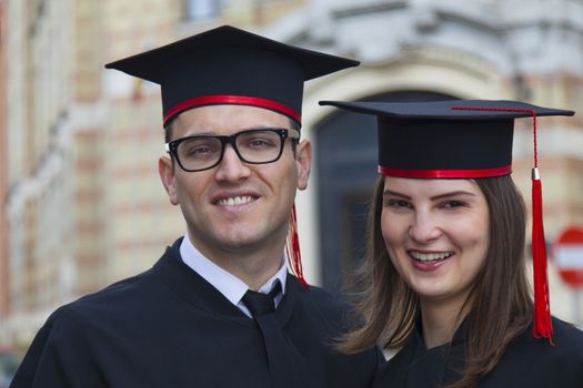 Outdoor portrait of a young couple of students in the graduation day near the university building.